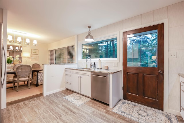 kitchen featuring light stone counters, a sink, light wood finished floors, dishwasher, and hanging light fixtures