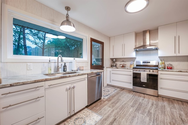 kitchen with wall chimney range hood, a sink, white cabinets, light wood-style floors, and stainless steel appliances