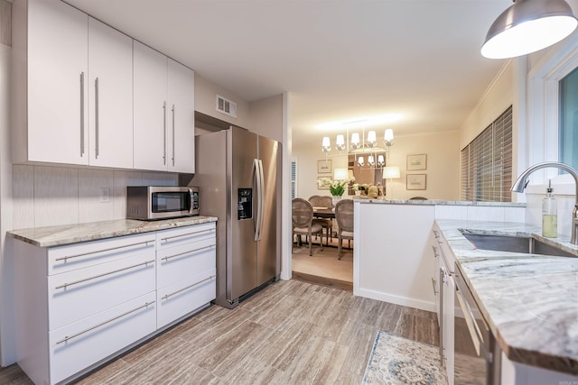 kitchen with an inviting chandelier, a sink, stainless steel appliances, light wood-type flooring, and visible vents
