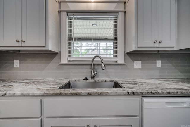 kitchen featuring decorative backsplash, white dishwasher, white cabinetry, light stone counters, and a sink