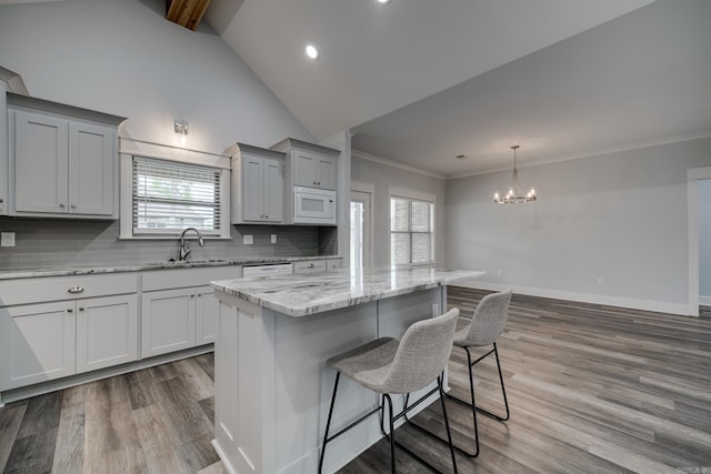 kitchen featuring a breakfast bar, a sink, white appliances, decorative backsplash, and wood finished floors