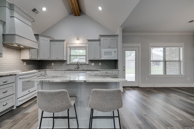 kitchen featuring visible vents, white appliances, a kitchen bar, gray cabinets, and backsplash