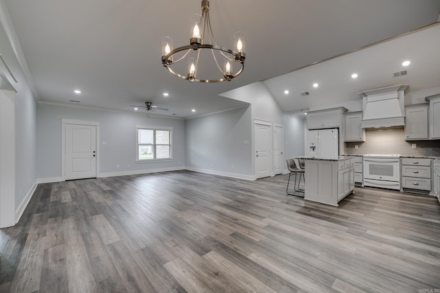 kitchen featuring white appliances, ceiling fan with notable chandelier, a kitchen bar, visible vents, and custom exhaust hood