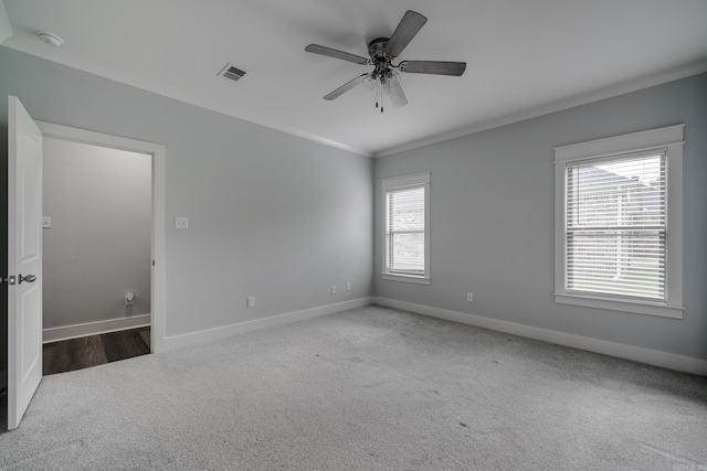 empty room with carpet flooring, crown molding, a ceiling fan, baseboards, and visible vents