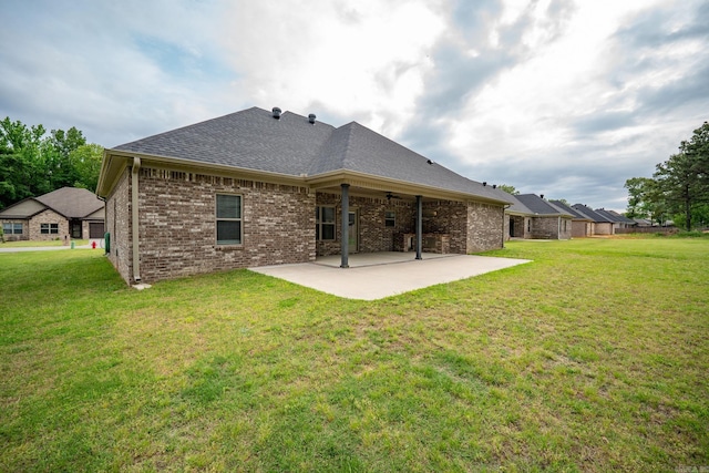 back of house featuring a patio, a shingled roof, a lawn, and brick siding