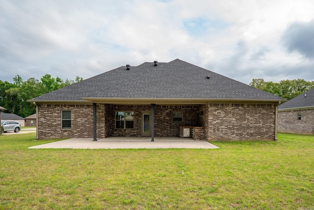 rear view of property with a yard, brick siding, a shingled roof, and a patio area