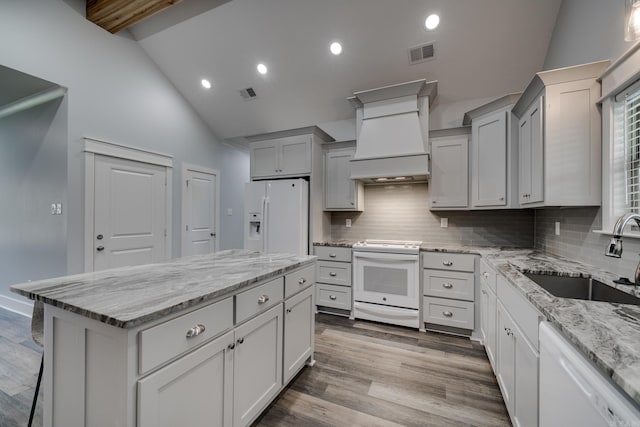 kitchen with visible vents, custom exhaust hood, a kitchen island, white appliances, and a sink