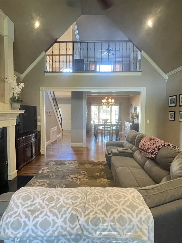 living room with crown molding, wood finished floors, high vaulted ceiling, a notable chandelier, and stairs