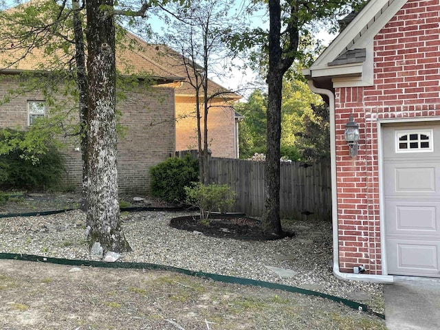 view of property exterior with brick siding, a garage, and fence