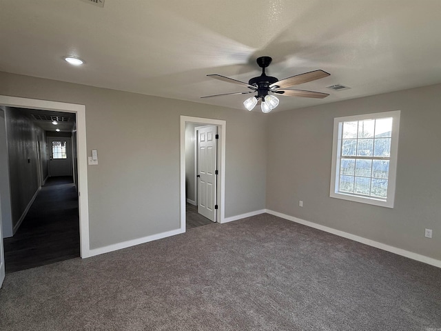 unfurnished room with ceiling fan, visible vents, baseboards, and dark colored carpet