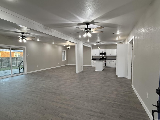 unfurnished living room featuring baseboards, ceiling fan, and dark wood-style floors