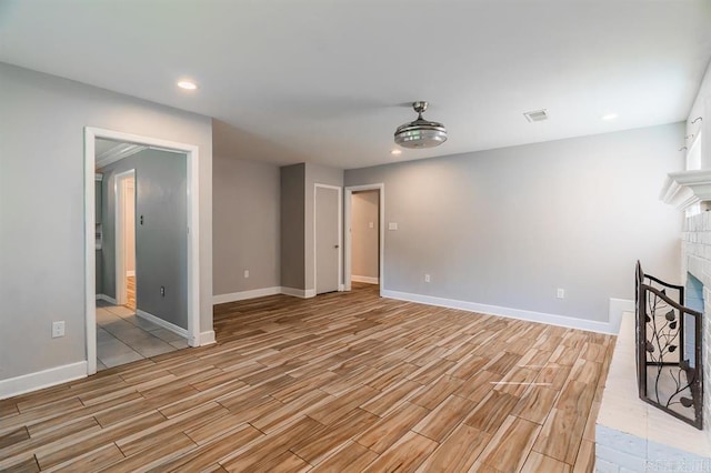 unfurnished living room featuring visible vents, light wood finished floors, a brick fireplace, and baseboards