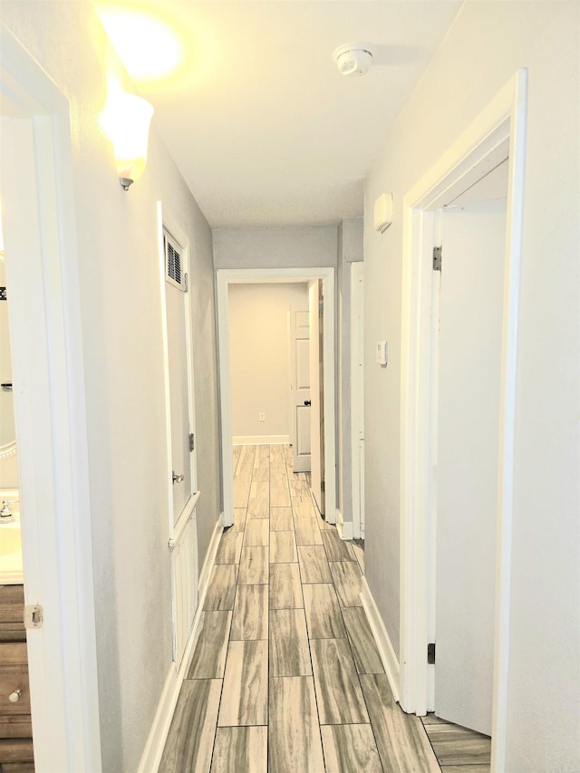 hallway with visible vents, wood tiled floor, and baseboards