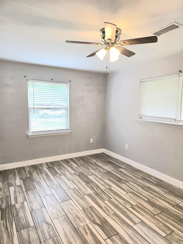empty room with baseboards, ceiling fan, wood finished floors, and visible vents