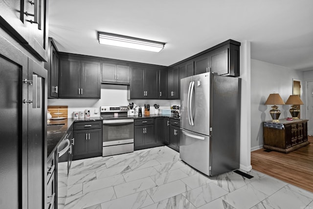 kitchen with dark countertops, baseboards, stainless steel appliances, and marble finish floor