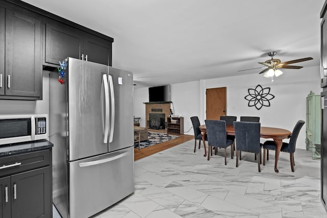 dining room with a brick fireplace, a ceiling fan, and marble finish floor