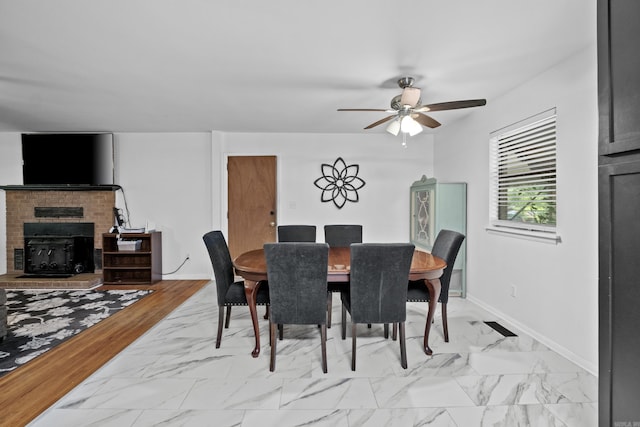 dining room featuring a brick fireplace, a ceiling fan, baseboards, and marble finish floor
