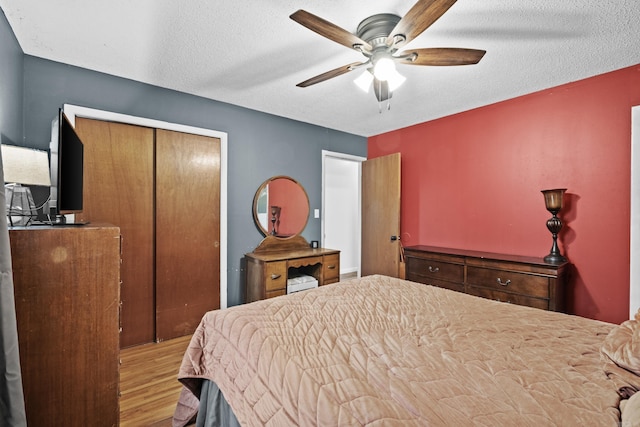 bedroom with a ceiling fan, a textured ceiling, wood finished floors, and a closet