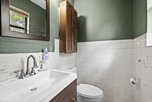 half bathroom featuring vanity, wainscoting, toilet, and tile walls