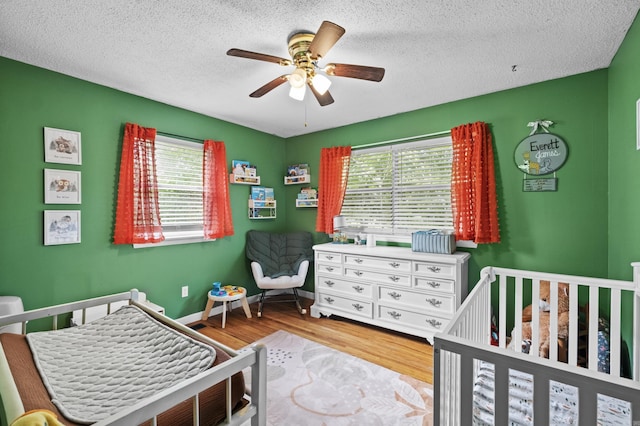 bedroom featuring a nursery area, baseboards, wood finished floors, and a textured ceiling