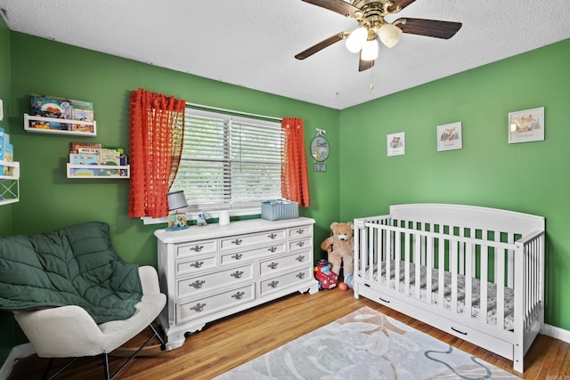 bedroom with a nursery area, ceiling fan, and wood finished floors