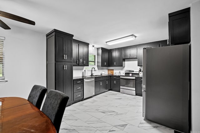 kitchen featuring ceiling fan, appliances with stainless steel finishes, dark countertops, a sink, and marble finish floor