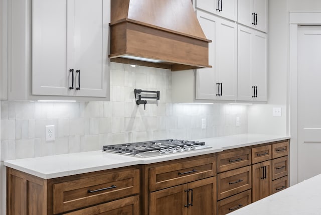 2940 Orchard View Dr, Conway, AR 72034 - kitchen featuring decorative backsplash, brown cabinets, white cabinets, custom range hood, and stainless steel gas stovetop