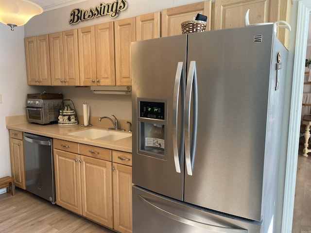 kitchen featuring stainless steel appliances, a sink, light wood finished floors, light countertops, and light brown cabinets