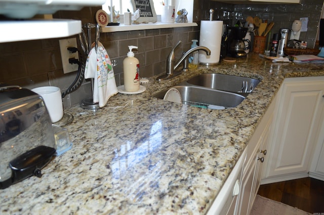 kitchen featuring light stone countertops, a sink, white cabinetry, wood finished floors, and backsplash