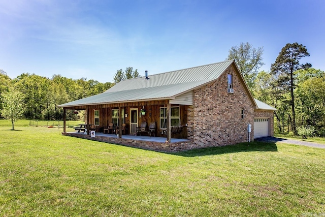 back of house featuring driveway, a lawn, a garage, and metal roof