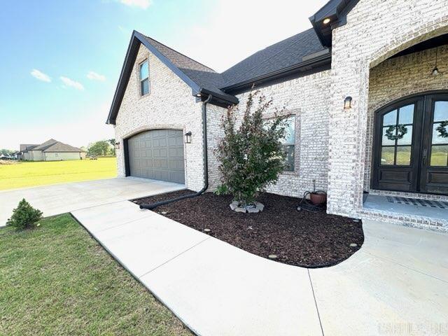 exterior space with an attached garage, brick siding, concrete driveway, french doors, and a yard