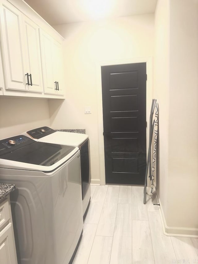 laundry area with baseboards, washer and clothes dryer, cabinet space, and light wood-type flooring