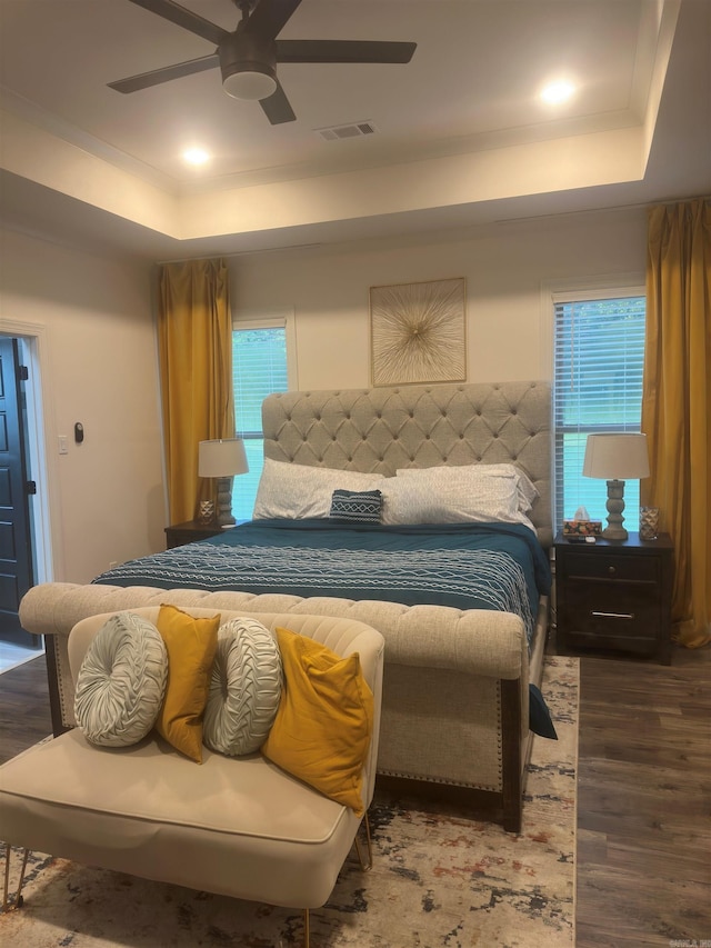 bedroom with ceiling fan, a tray ceiling, wood finished floors, and visible vents