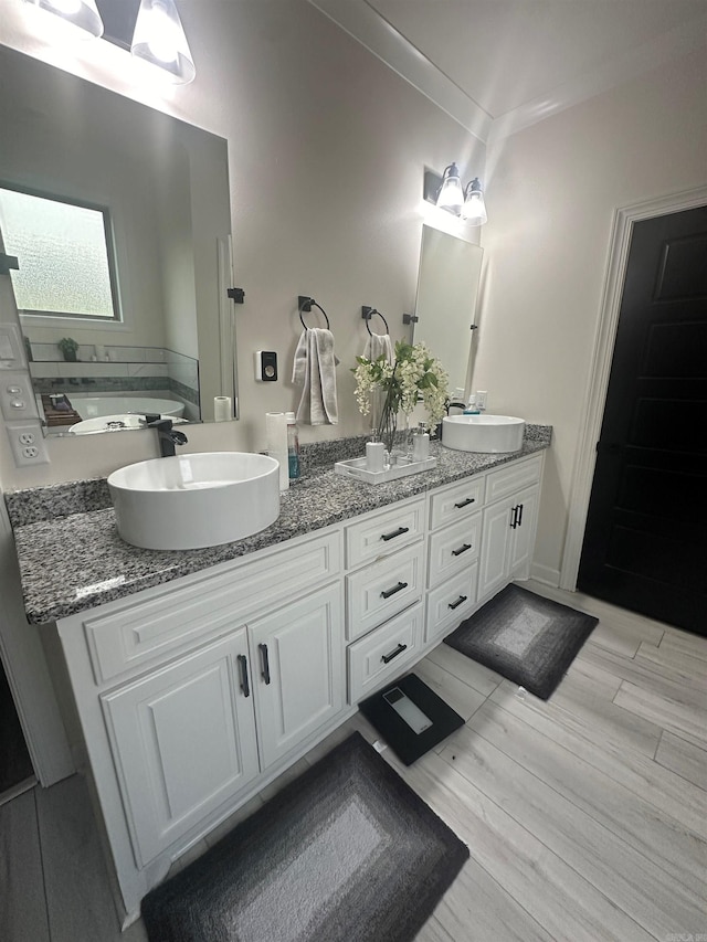bathroom with double vanity, a sink, wood finished floors, and a washtub