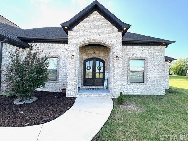 entrance to property featuring a yard, brick siding, french doors, and a shingled roof