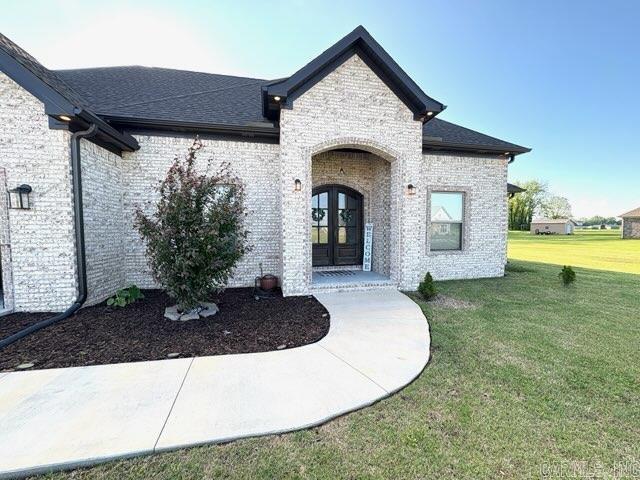entrance to property featuring brick siding, roof with shingles, a yard, and french doors