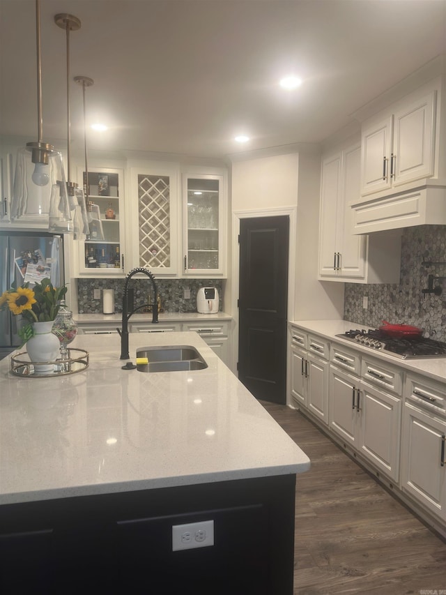 kitchen featuring a sink, stainless steel gas cooktop, glass insert cabinets, and tasteful backsplash