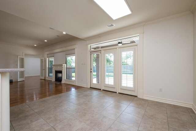 unfurnished living room with a glass covered fireplace, baseboards, light tile patterned floors, visible vents, and ornamental molding