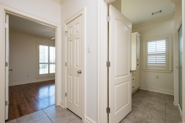 hallway featuring visible vents, ornamental molding, baseboards, and light tile patterned flooring