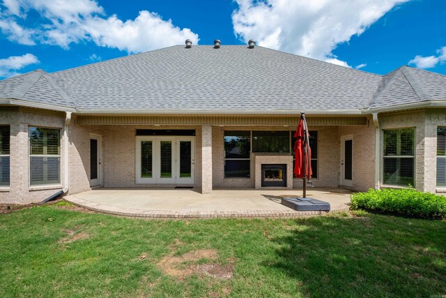 back of house featuring a shingled roof, a fireplace, brick siding, a patio, and a yard