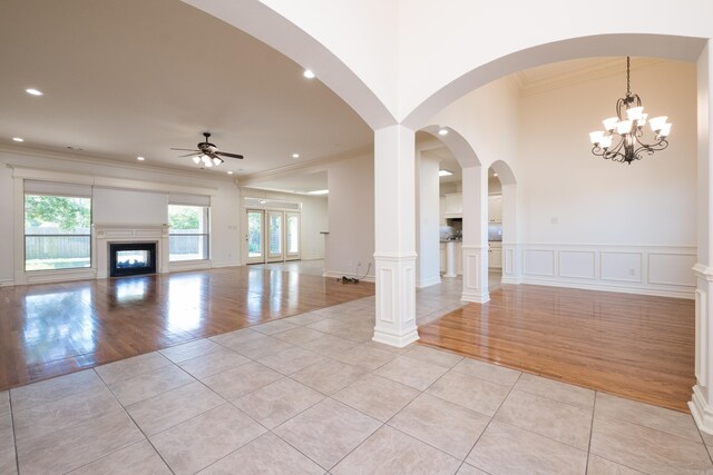 unfurnished living room featuring crown molding, light tile patterned flooring, a glass covered fireplace, and ceiling fan with notable chandelier