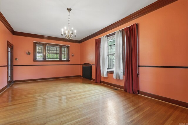 empty room with light wood-style floors, ornamental molding, baseboards, and a chandelier