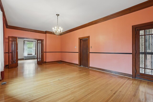 empty room featuring crown molding, a notable chandelier, light wood-style flooring, and radiator