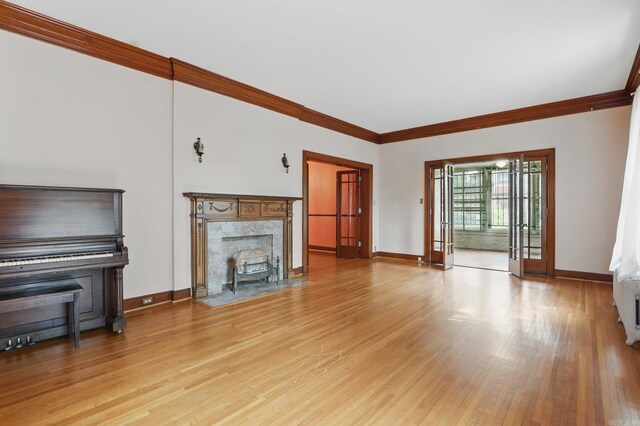 unfurnished living room with baseboards, ornamental molding, and light wood-type flooring
