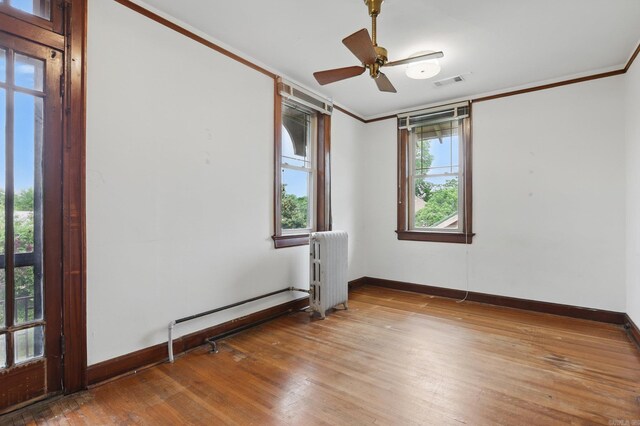 spare room with radiator heating unit, baseboards, wood finished floors, visible vents, and ornamental molding