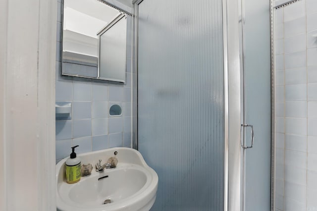 bathroom featuring a sink, a stall shower, and tile walls