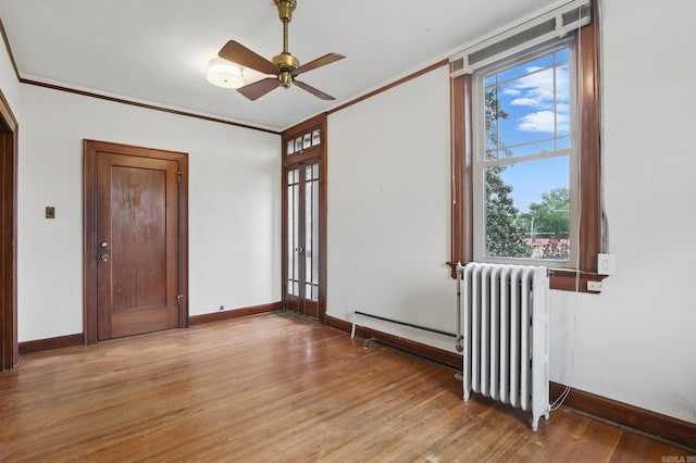 unfurnished room featuring ceiling fan, crown molding, baseboards, radiator, and light wood-style flooring