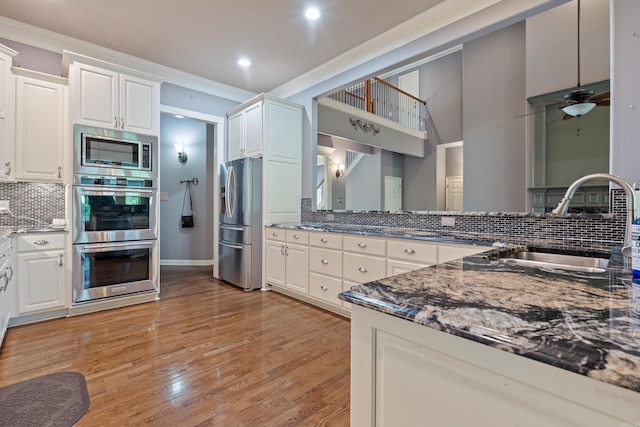 kitchen with crown molding, a sink, dark stone counters, stainless steel appliances, and tasteful backsplash