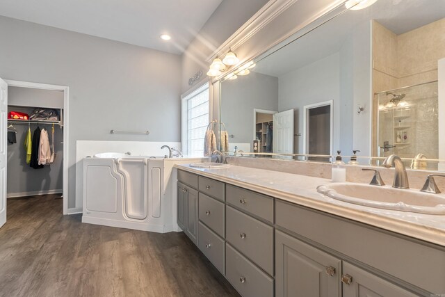 bathroom featuring a sink, a bath, wood finished floors, and tiled shower