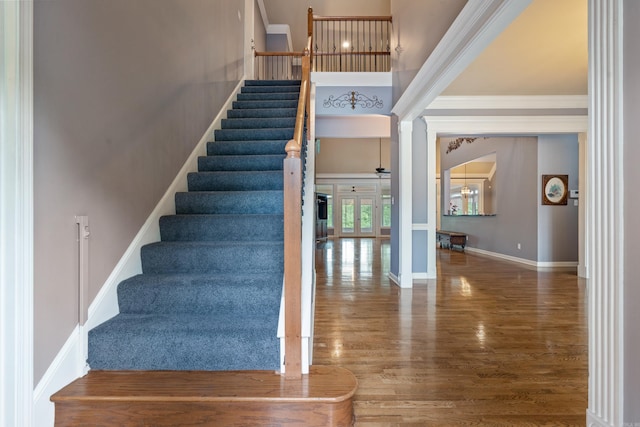 stairs with baseboards, ornamental molding, wood finished floors, and a towering ceiling